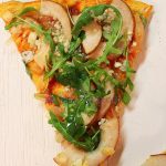 PREPARACIÓN: En un sartén con el aceite freír la cebolla por unos 4 minutos, luego agregar el azúcar y dejar cocinar a fuego medio por unos 4 minutos más apróximadamente. Cuando la masa de la pizza este pre-cocida, cubrir con la cebolla caramelizada, luego colocar las rodajas de peras y esparcir el queso azúl. Llevar al horno por unos 10 minutos a 400°F (200°C). Retirar del horno y cubrir con rúcula.